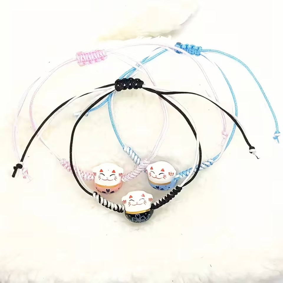 un bracelet en tissu en forme d'un maneki neko coloré. Symbole de chance, de bonne fortune, il est inspiré du style japonais