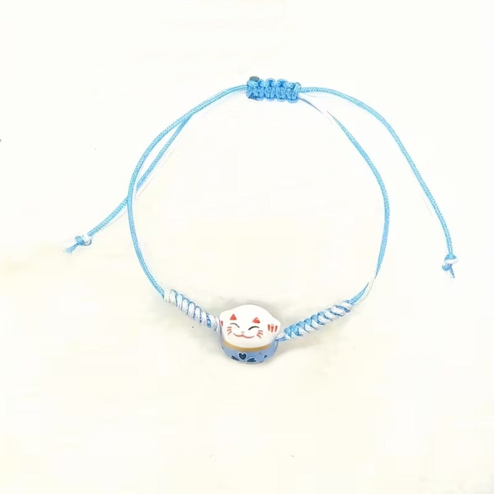 un bracelet en tissu en forme d'un maneki neko coloré. Symbole de chance, de bonne fortune, il est inspiré du style japonais