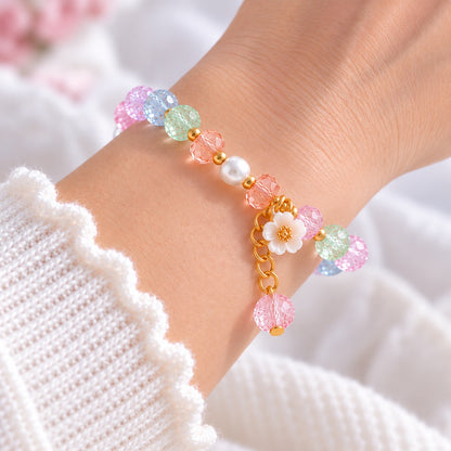 Bracelet femme élégant en perles transparentes effet craquelé, orné de perles nacrées, cristaux multicolores et détails dorés. Délicate fleur de sakura blanche avec pendentif scintillant, porté au poignet d'une femme. Bijou romantique et féminin au style japonais kawaii, idéal pour une touche douce et raffinée au quotidien.