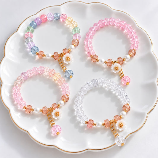 Lot de 4 bracelets kawaii en perles craquelées scintillantes, aux couleurs rose, blanc transparent et multicolore pastel. Ornées de délicates fleurs de sakura, de perles nacrées et de pendentifs dorés, ces bijoux féminins au style japonais romantique sont présentés sur une jolie coupelle blanche.