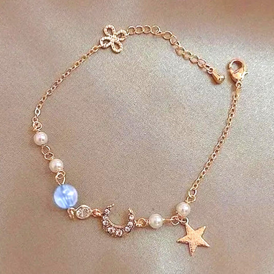 un bracelet doré élégant qui rappelle le mystère et la brillance de la galaxie. Il est composé d'un croissant de lune tout en strass, d'une étoile et de perles blanches et d'une bleue.
