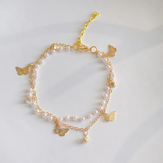 un superbe bracelet doré composé de deux chaines complémentaires. La première est faite de perles blanches et la deuxième est orné de papillons doré et de strass scintillants. L'ensemble est chic et bohème.