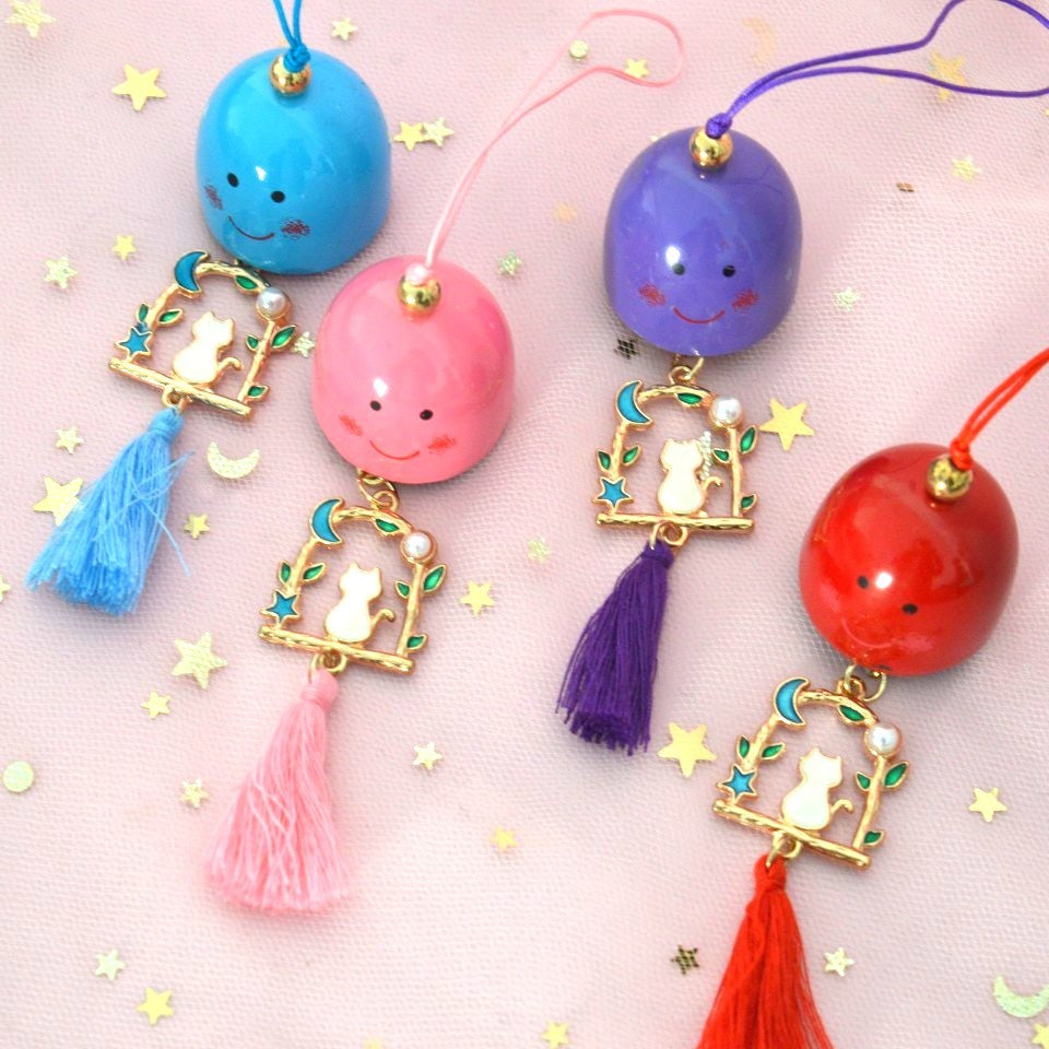un carillon avec une clochette expression kawaii, une breloque en forme de chat qui est sur une balançoire y est suspendu, et un pompon coloré finit l'ensemble.