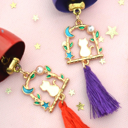 un carillon avec une clochette expression kawaii, une breloque en forme de chat qui est sur une balançoire y est suspendu, et un pompon coloré finit l'ensemble.