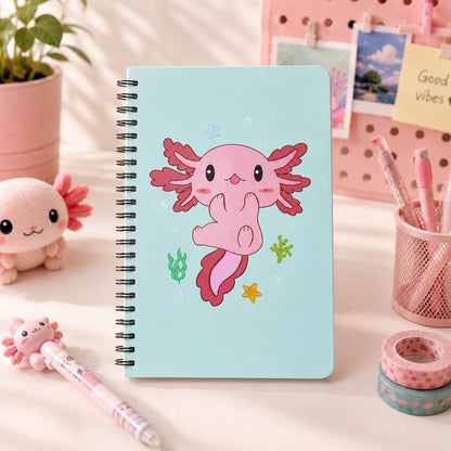 Carnet à spirales axolotl kawaii bleu pastel avec illustration d’un axolotl rose, présenté dans un décor de bureau mignon avec papeterie rose.
