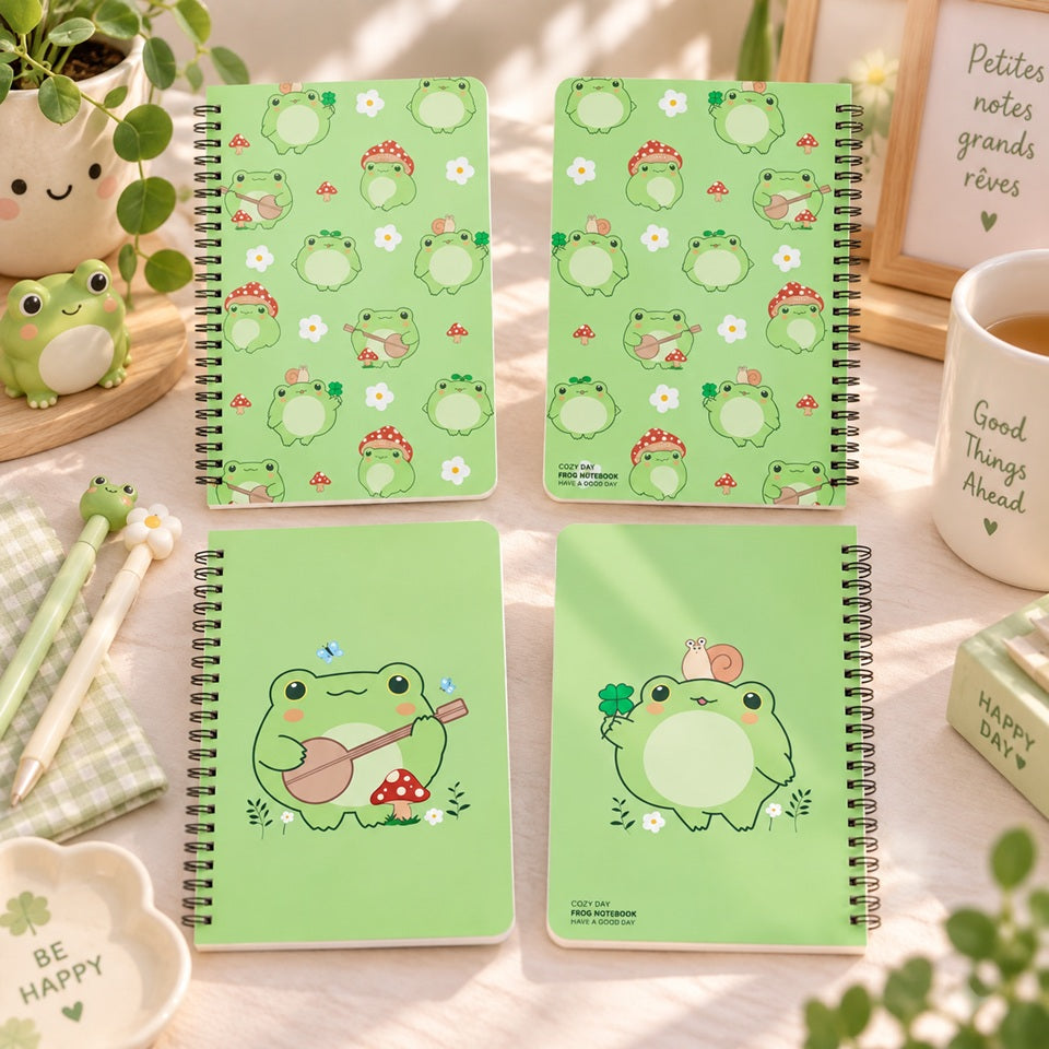 Carnets à spirales verts décorés d’adorables grenouilles kawaii, champignons et petites fleurs, présentés dans un joli décor de papeterie aux tons pastel.