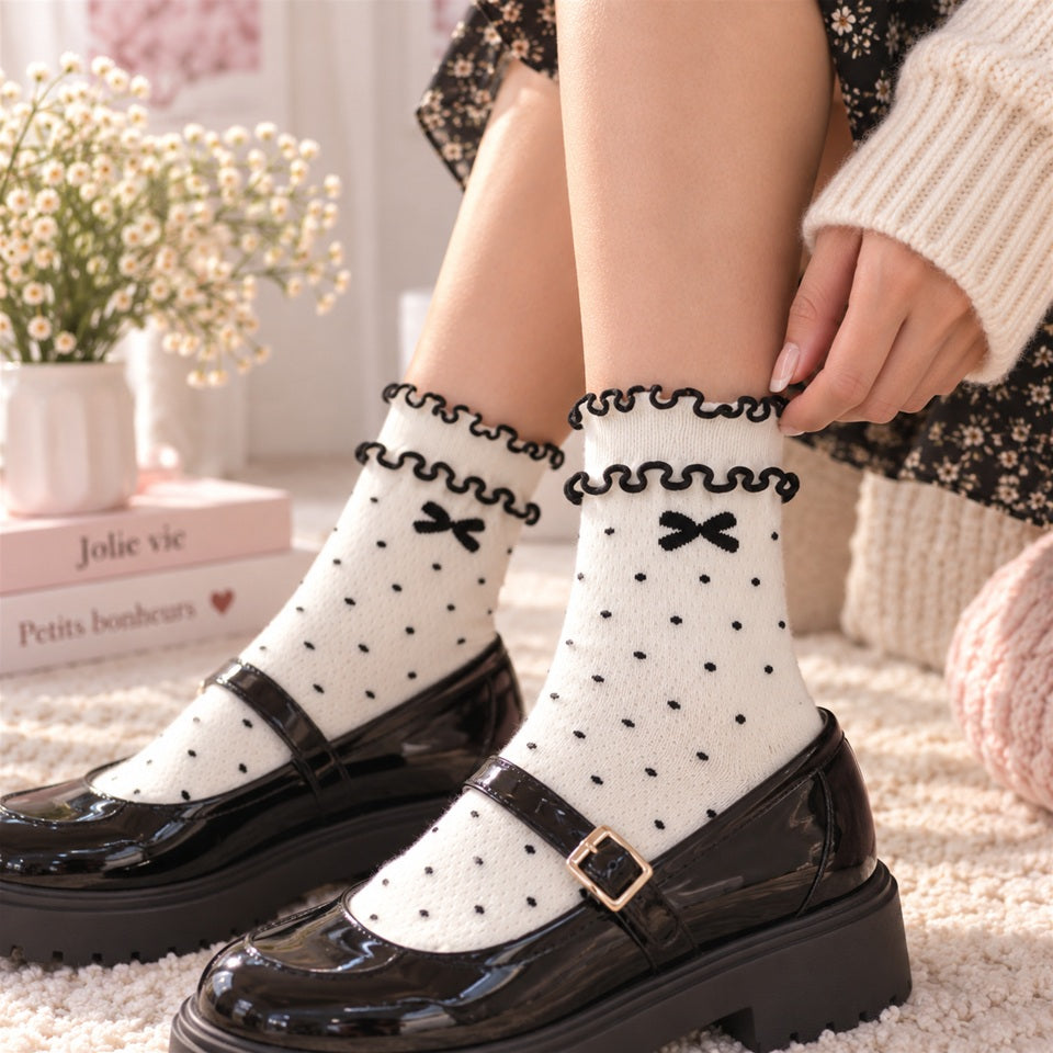 Femme portant des chaussettes blanches à pois noirs avec petits nœuds et double froufrou, associées à des chaussures noires élégantes.