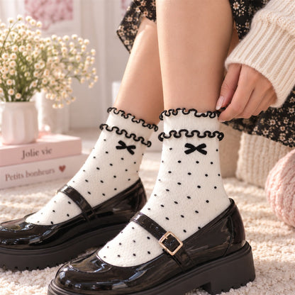 Femme portant des chaussettes blanches à pois noirs avec petits nœuds et double froufrou, associées à des chaussures noires élégantes.