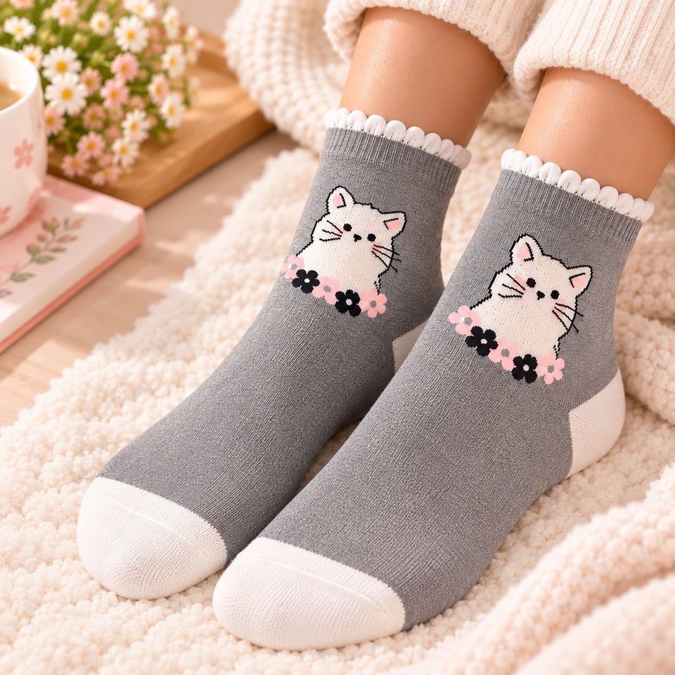 Chaussettes grises kawaii portées aux pieds, décorées d’un adorable chat blanc entouré de petites fleurs roses et noires, dans une ambiance douce et cosy