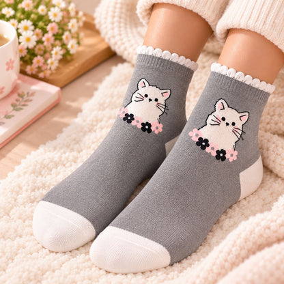 Chaussettes grises kawaii portées aux pieds, décorées d’un adorable chat blanc entouré de petites fleurs roses et noires, dans une ambiance douce et cosy