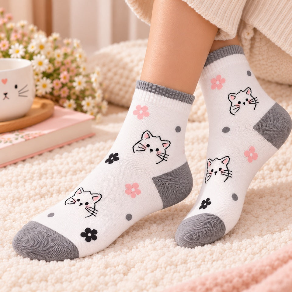 Chaussettes blanches kawaii pour femme, décorées de petits chats, fleurs roses et noires et pois gris, portées aux pieds dans une ambiance douce et cosy.