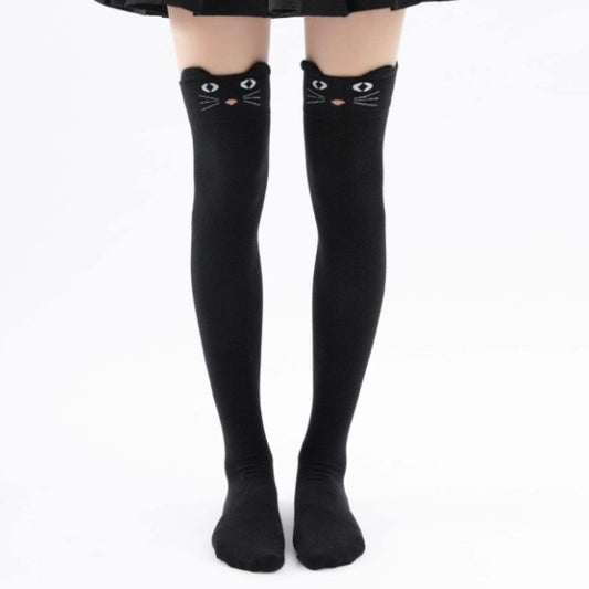 une paire de chaussettes hautes noires sur lesquelles est brodé un visage de chat avec ses moustaches. Elles ont deux petites oreilles qui dépassent du haut de la chaussette
