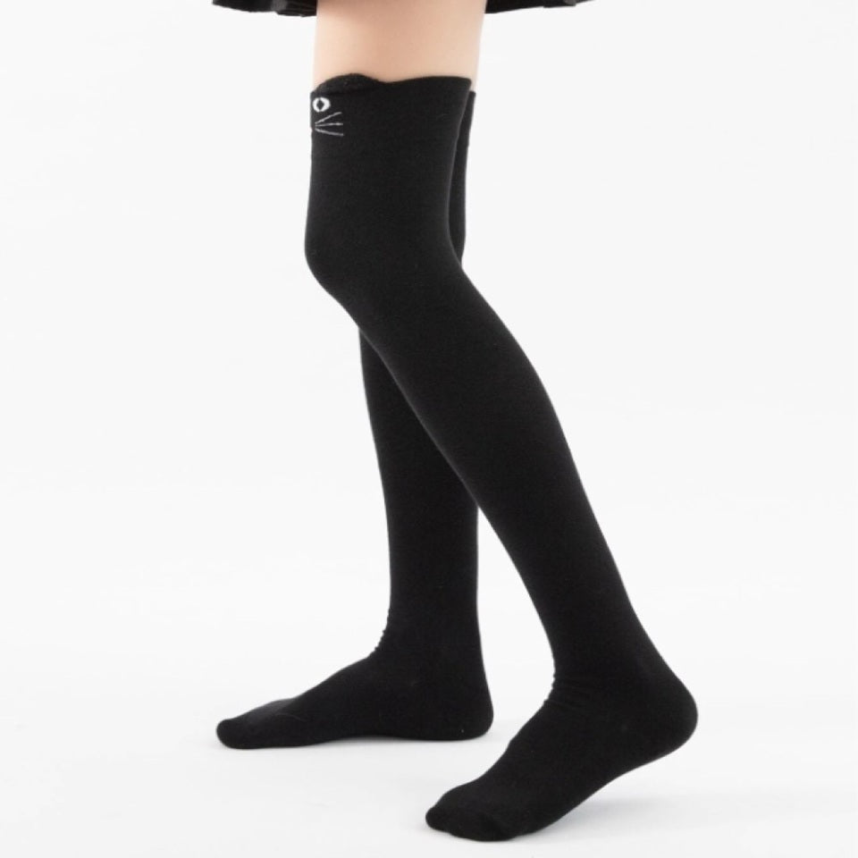 une paire de chaussettes hautes noires sur lesquelles est brodé un visage de chat avec ses moustaches. Elles ont deux petites oreilles qui dépassent du haut de la chaussette