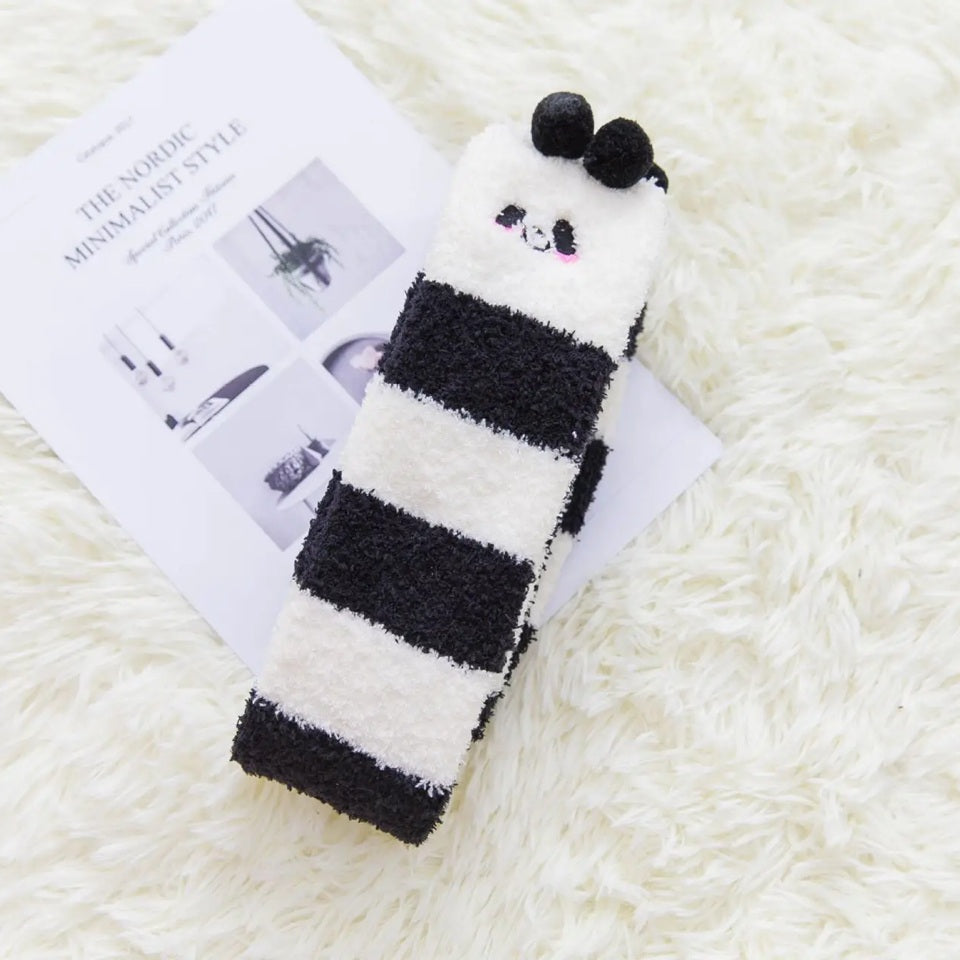 des chaussettes hautes en matière pilou toutes douces rayées noires et blanches. Sur le haut des chaussettes, un visage mignon de panda avec ses joues roses et deux pompons noirs en guise d'oreilles