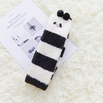 des chaussettes hautes en matière pilou toutes douces rayées noires et blanches. Sur le haut des chaussettes, un visage mignon de panda avec ses joues roses et deux pompons noirs en guise d'oreilles