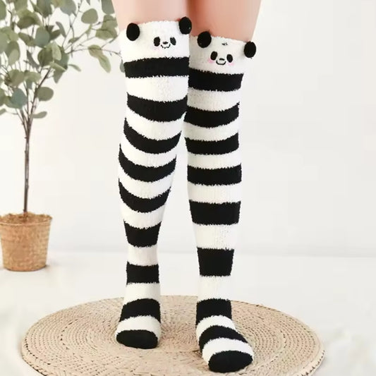 des chaussettes hautes en matière pilou toutes douces rayées noires et blanches. Sur le haut des chaussettes, un visage mignon de panda avec ses joues roses et deux pompons noirs en guise d'oreilles
