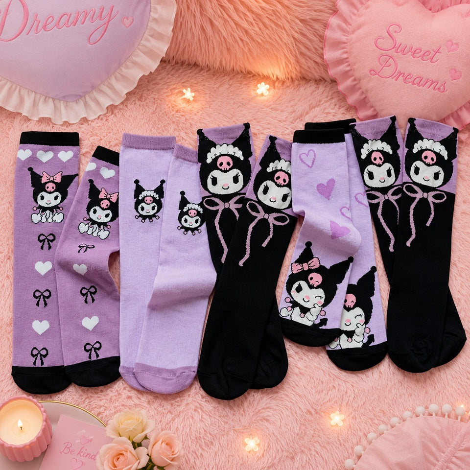 Des paires de chaussettes Kuromi dans des tons violet et noir, soigneusement disposées sur un tapis en fausse fourrure rose. Les différents modèles présentent des motifs de Kuromi, de petits cœurs et des nœuds. L'ensemble est entouré d'une décoration féminine et cosy comprenant des coussins en forme de cœur, une bougie parfumée, des fleurs, une guirlande lumineuse et des accessoires pastel, créant une ambiance douce, chaleureuse et kawaii.