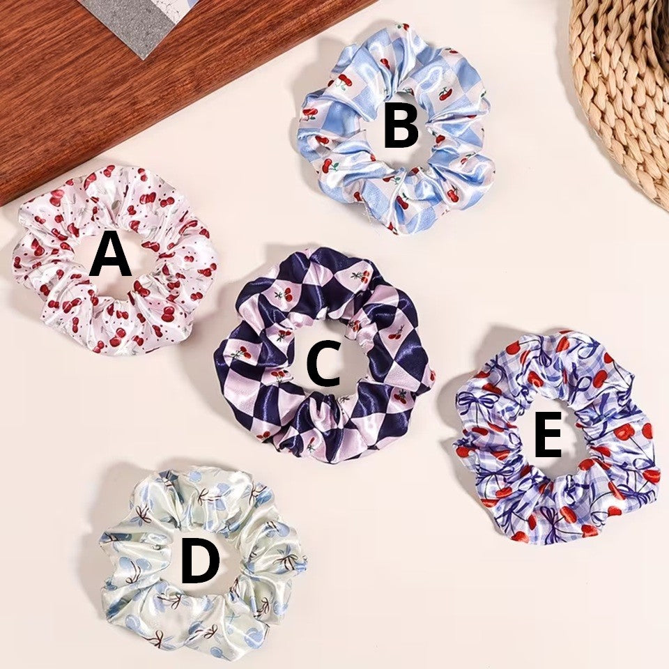 Une collection de chouchous satinés de couleur bleu et blanc à motif de cerises. Leur texture brillante est mise en valeur dans un intérieur lumineux aux tons neutres avec un arrière-plan clair.
