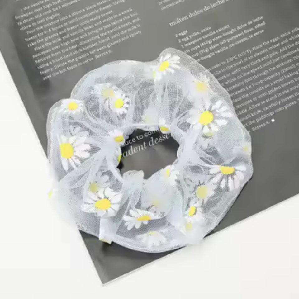 un chouchou en organza blanc  joliment présenté, posé sur une feuille sur une table blanche.