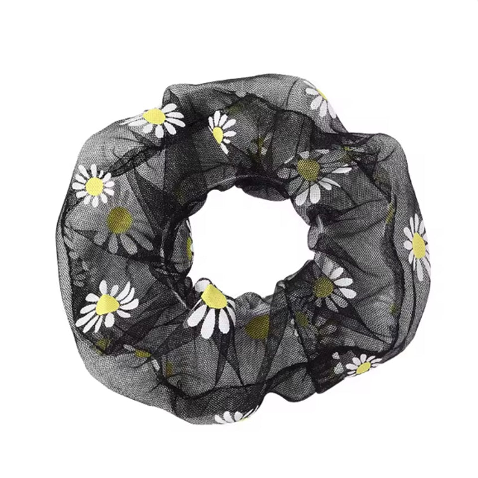 un chouchou en organza noir  joliment présenté, posé sur une feuille sur une table blanche.