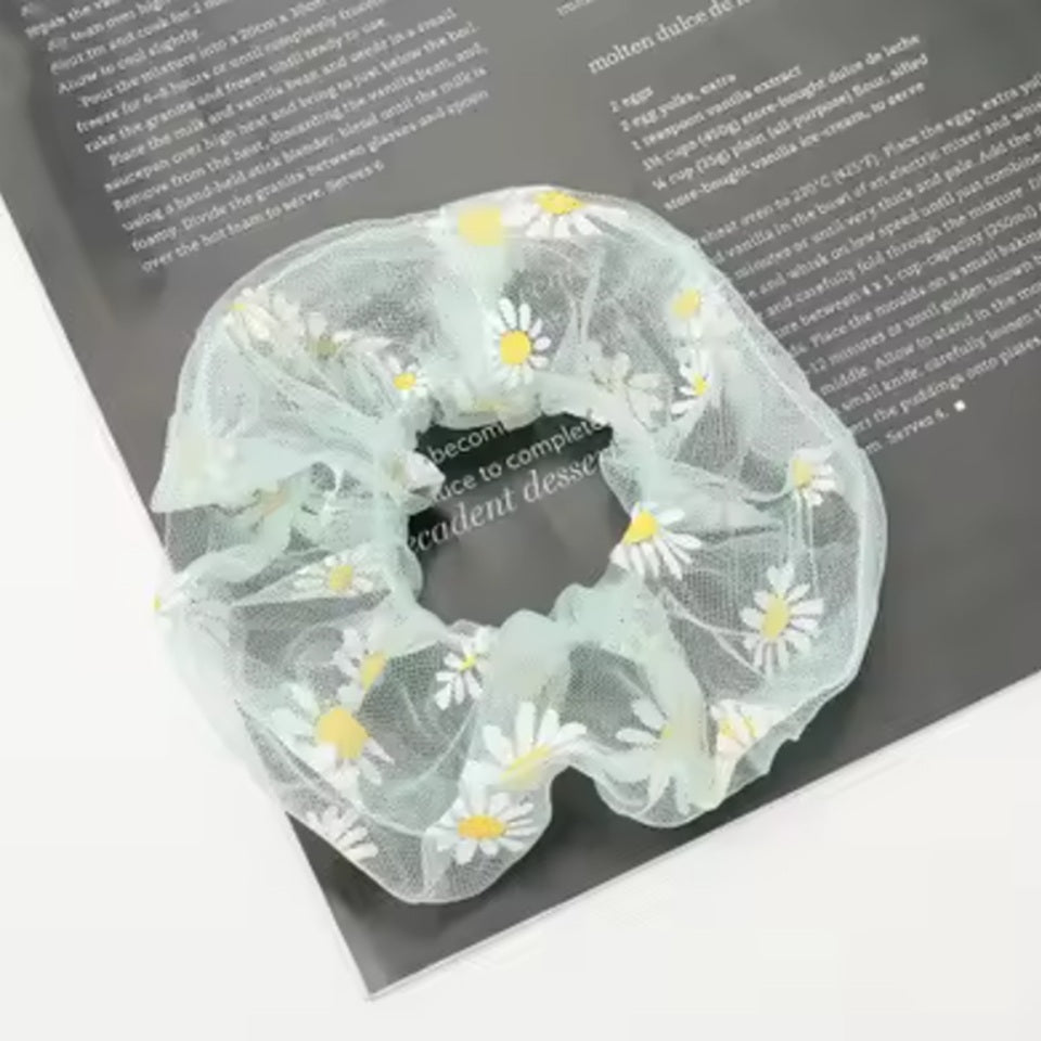 un chouchou en organza vert  joliment présenté, posé sur une feuille sur une table blanche.