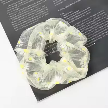 un chouchou en organza jaune joliment présenté, posé sur une feuille sur une table blanche.
