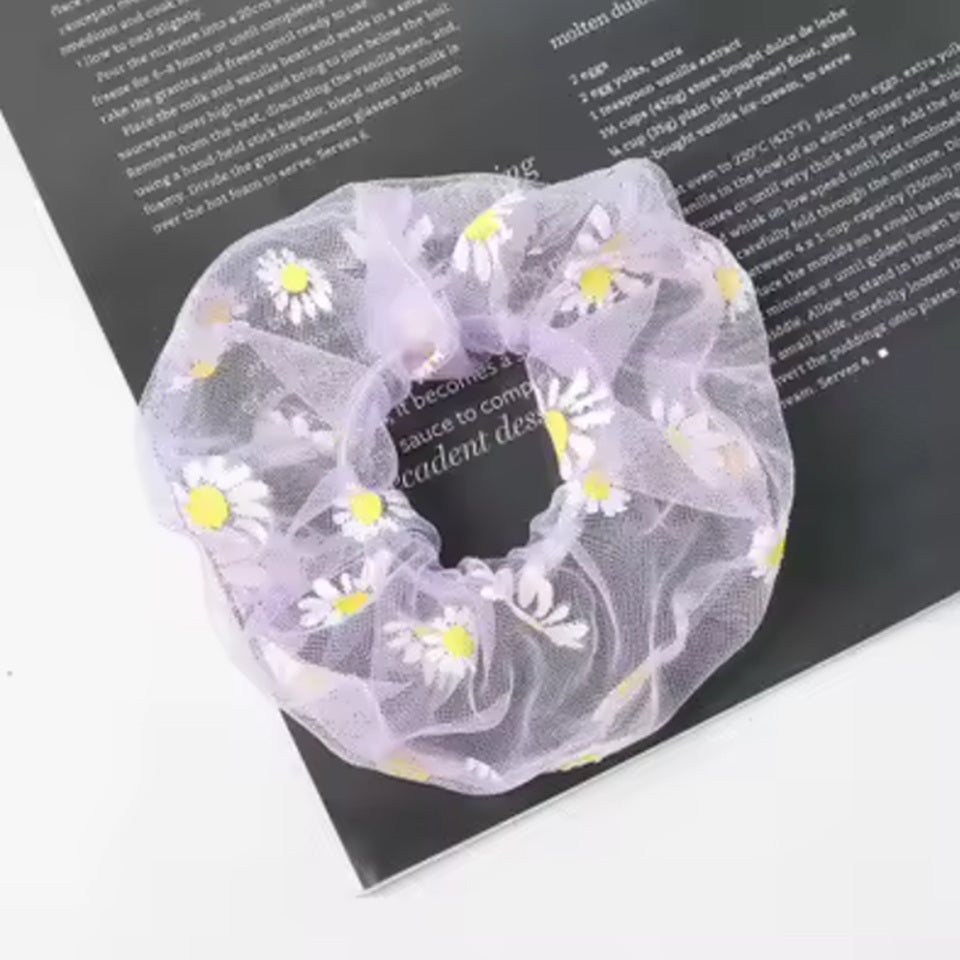 un chouchou en organza mauve joliment présenté, posé sur une feuille sur une table blanche.