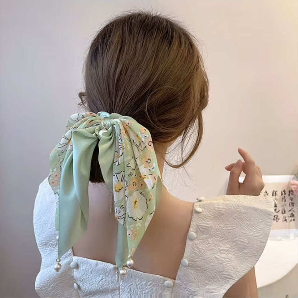 des chouchous foulards vert, beige et noir aux motifs fleuris et aux couleurs unies. De jolies perles blanches finissent de compléter l'ensemble pour un résultat féminin, romantique et élégant.