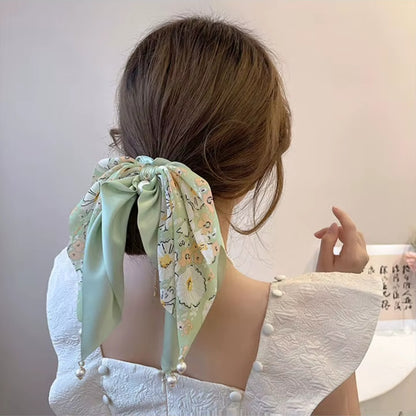 des chouchous foulards vert, beige et noir aux motifs fleuris et aux couleurs unies. De jolies perles blanches finissent de compléter l'ensemble pour un résultat féminin, romantique et élégant.