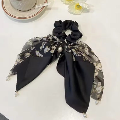 des chouchous foulards vert, beige et noir aux motifs fleuris et aux couleurs unies. De jolies perles blanches finissent de compléter l'ensemble pour un résultat féminin, romantique et élégant.