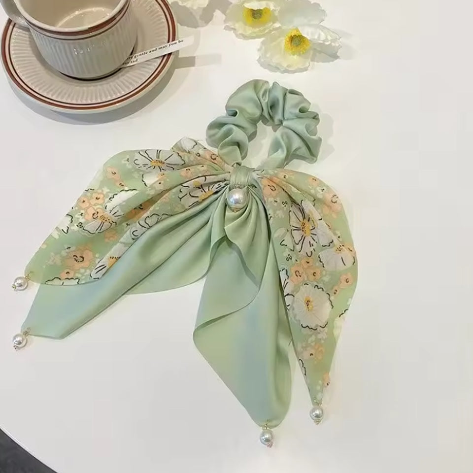 des chouchous foulards vert, beige et noir aux motifs fleuris et aux couleurs unies. De jolies perles blanches finissent de compléter l'ensemble pour un résultat féminin, romantique et élégant.