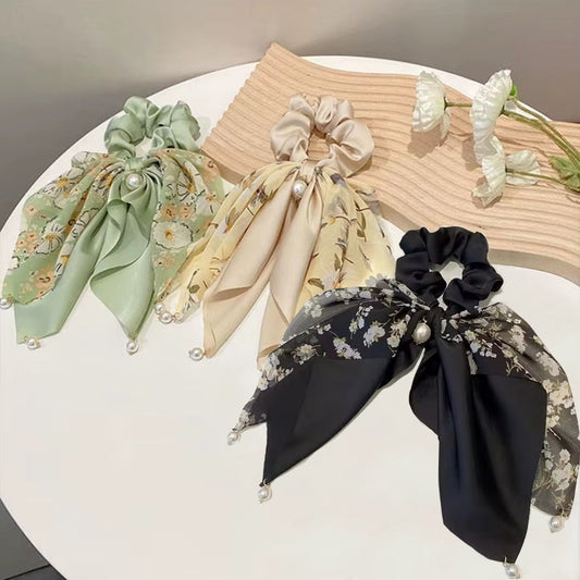 des chouchous foulards vert, beige et noir aux motifs fleuris et aux couleurs unies. De jolies perles blanches finissent de compléter l'ensemble pour un résultat féminin, romantique et élégant.