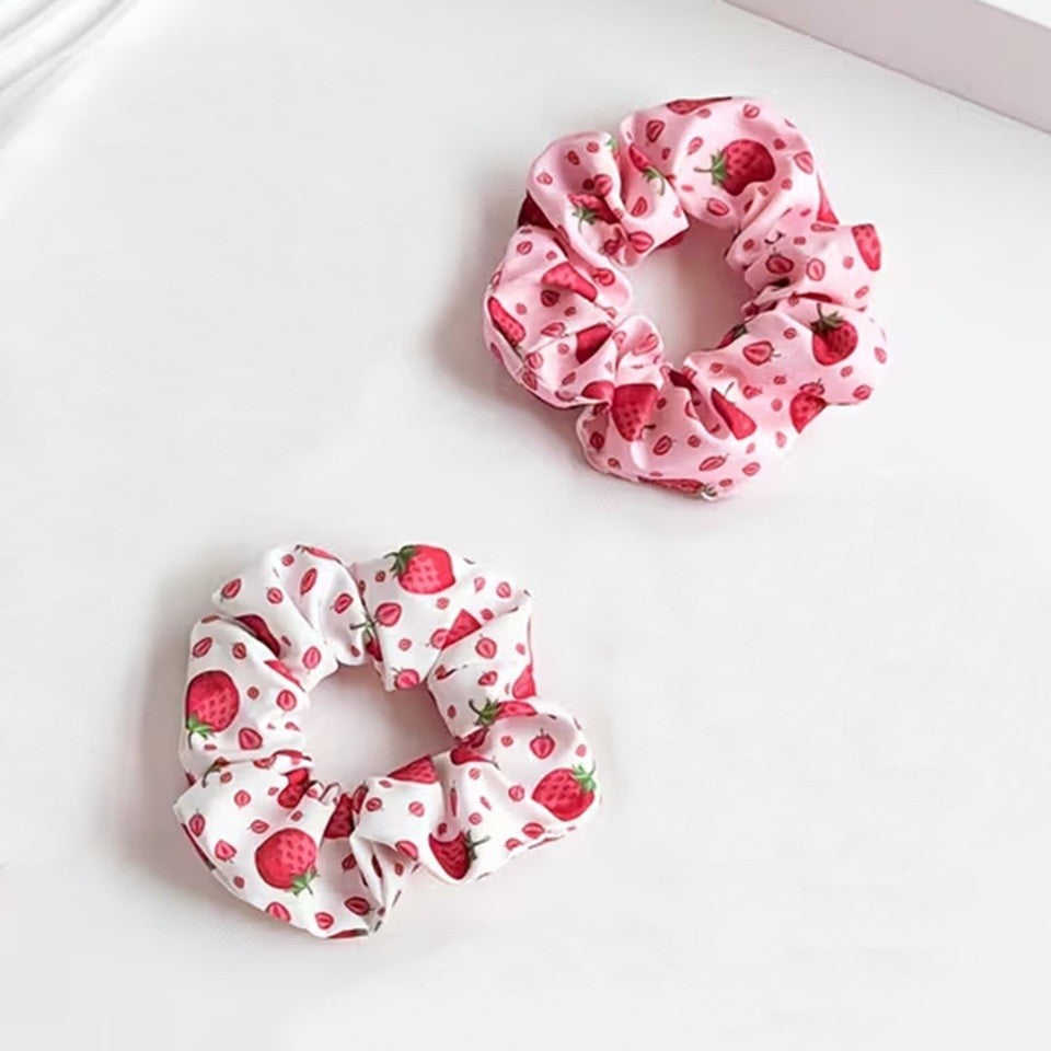 Deux chouchous blanc et rose au motif de fraises rouges gourmandes et fraiches posés sur une table blanche. Look  mignon et tendance fruitée adorable.
