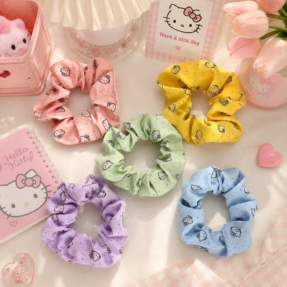 Lot de chouchous Hello Kitty colorés en tissu, présentés dans une mise en scène kawaii aux tons pastel avec carnet, fleurs et accessoires décoratifs. Ces élastiques pour cheveux roses, jaunes, verts, bleus et violets apportent une touche mignonne et colorée aux coiffures du quotidien.