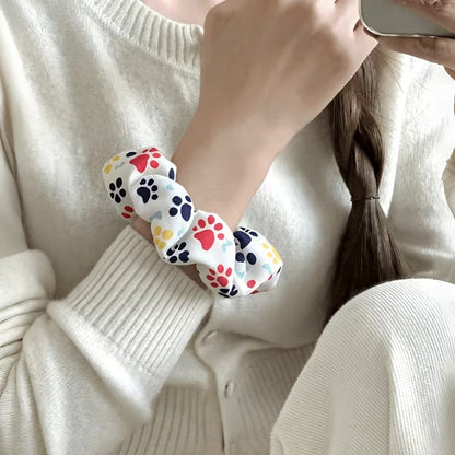 Une femme porte à son poignet un chouchou blanc au motif de pattes de chat multicolores hyper mignonnes.