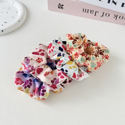 Des chouchous colorés au motif de pattes d'animaux multicolores sont alignés sur une table blanche. Design hyper mignon, parfait pour les amoureux des animaux.