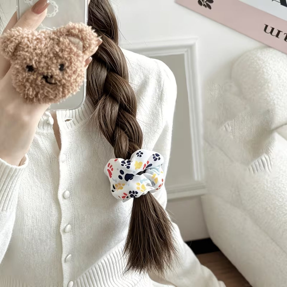 Une femme porte un chouchou blanc au motif de pattes d'animaux colorées. Elle a une tresse qu'elle a attaché avec le chouchou. Style mignon et adorable !