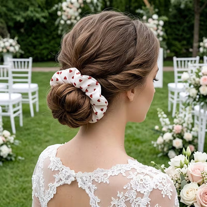 Une femme porte dans les cheveux, un chouchou blanc au motif de coeurs rouges. Il habille avec élégance et délicatesse son chignon.