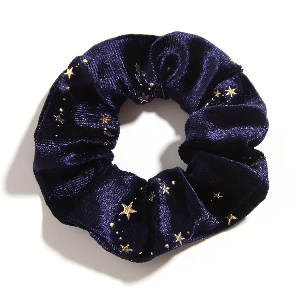 Gros plan d'un chouchou en matière velours bleu marine et au motif d'étoiles dorées. Super doux et élégant, il habille avec délicatesse et enchantement n'importe quelle coiffure.