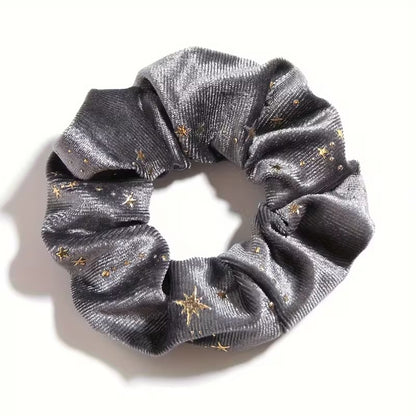 Gros plan d'un chouchou en matière velours gris et au motif d'étoiles dorées. Super doux et élégant, il habille avec délicatesse et enchantement n'importe quelle coiffure.
