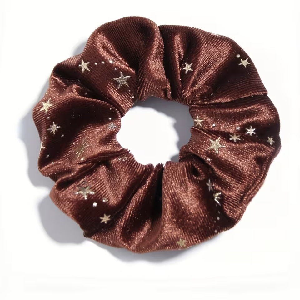 Gros plan d'un chouchou en matière velours marron et au motif d'étoiles dorées. Super doux et élégant, il habille avec délicatesse et enchantement n'importe quelle coiffure.