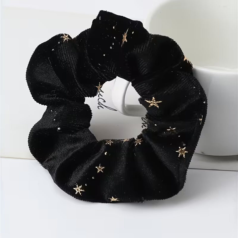 Gros plan d'un chouchou en matière velours noir et au motif d'étoiles dorées. Super doux et élégant, il habille avec délicatesse et enchantement n'importe quelle coiffure.