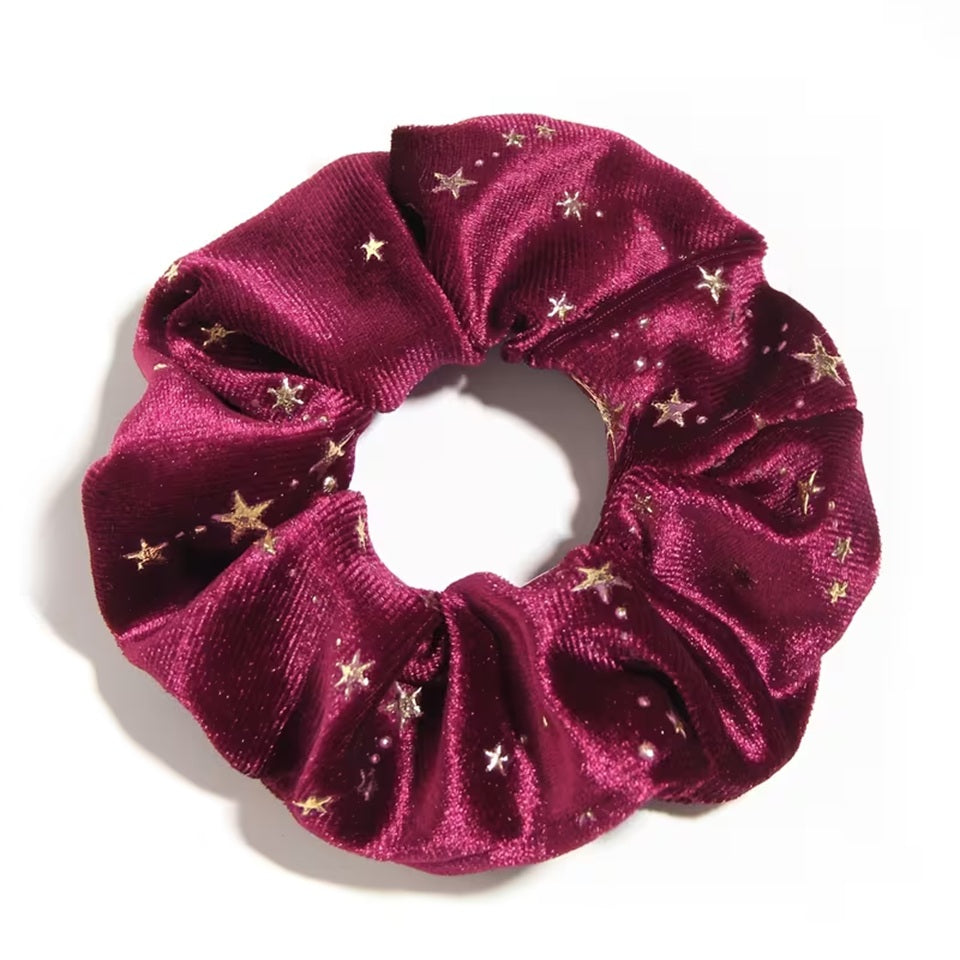 Gros plan d'un chouchou en matière velours prune et au motif d'étoiles dorées. Super doux et élégant, il habille avec délicatesse et enchantement n'importe quelle coiffure.