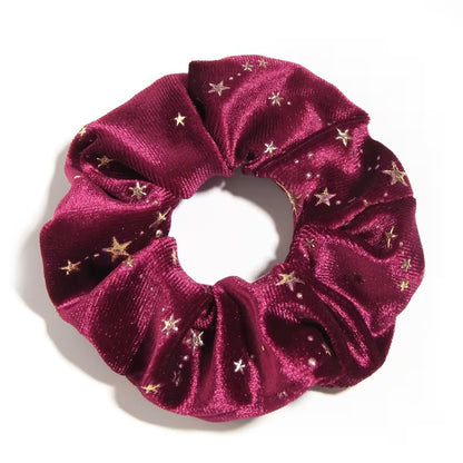 Gros plan d'un chouchou en matière velours prune et au motif d'étoiles dorées. Super doux et élégant, il habille avec délicatesse et enchantement n'importe quelle coiffure.