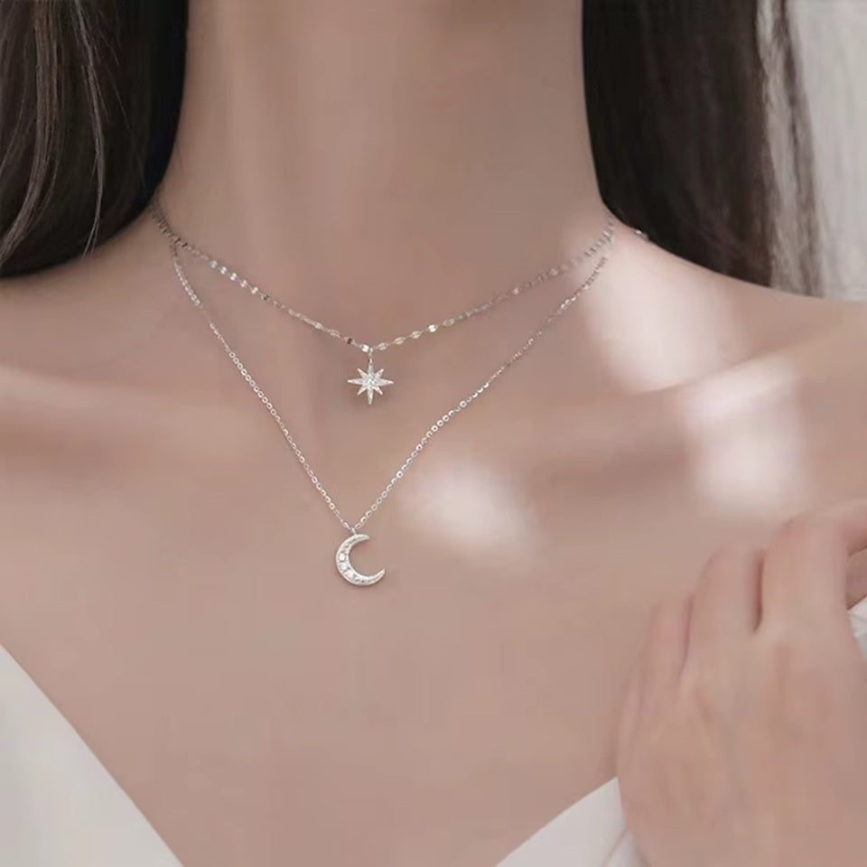 un collier composé de deux chaines argentées et de deux pendentifs tout en strass : une étoile et une lune.