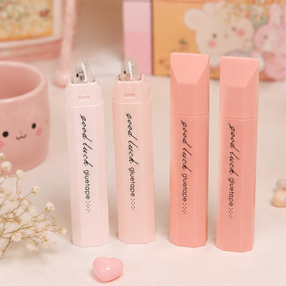 De la colle sous forme de ruban dans un joli étui rose. Ils sont posés sur une jolie table rose et mignonne, entourés d'articles kawaii.