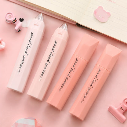 de la colle sous forme de ruban dans leur joli étui rose. Ils sont posés sur un bureau mignon.