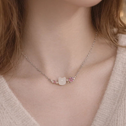 un superbe collier en acier inoxydable argenté composé d'une pierre blanche sculptée en forme de tête de chat, d'une fleur de sakura et d'un pétale rose et de petites perles blanches. L'ensemble est poétique, raffiné et plein de poésie.