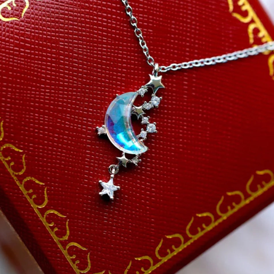 un bijou argentée dont le pendentif représente un croissant de lune aux reflets bleutés cristallins entourée de petites étoiles scintillantes