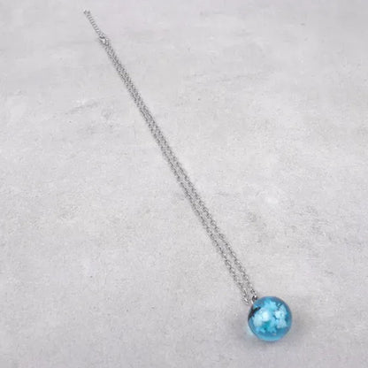 un joli collier argenté d'une sphère transparente et bleue renfermant un oiseau noir volant parmi des nuages comme si un bout de ciel y avait été capturé.